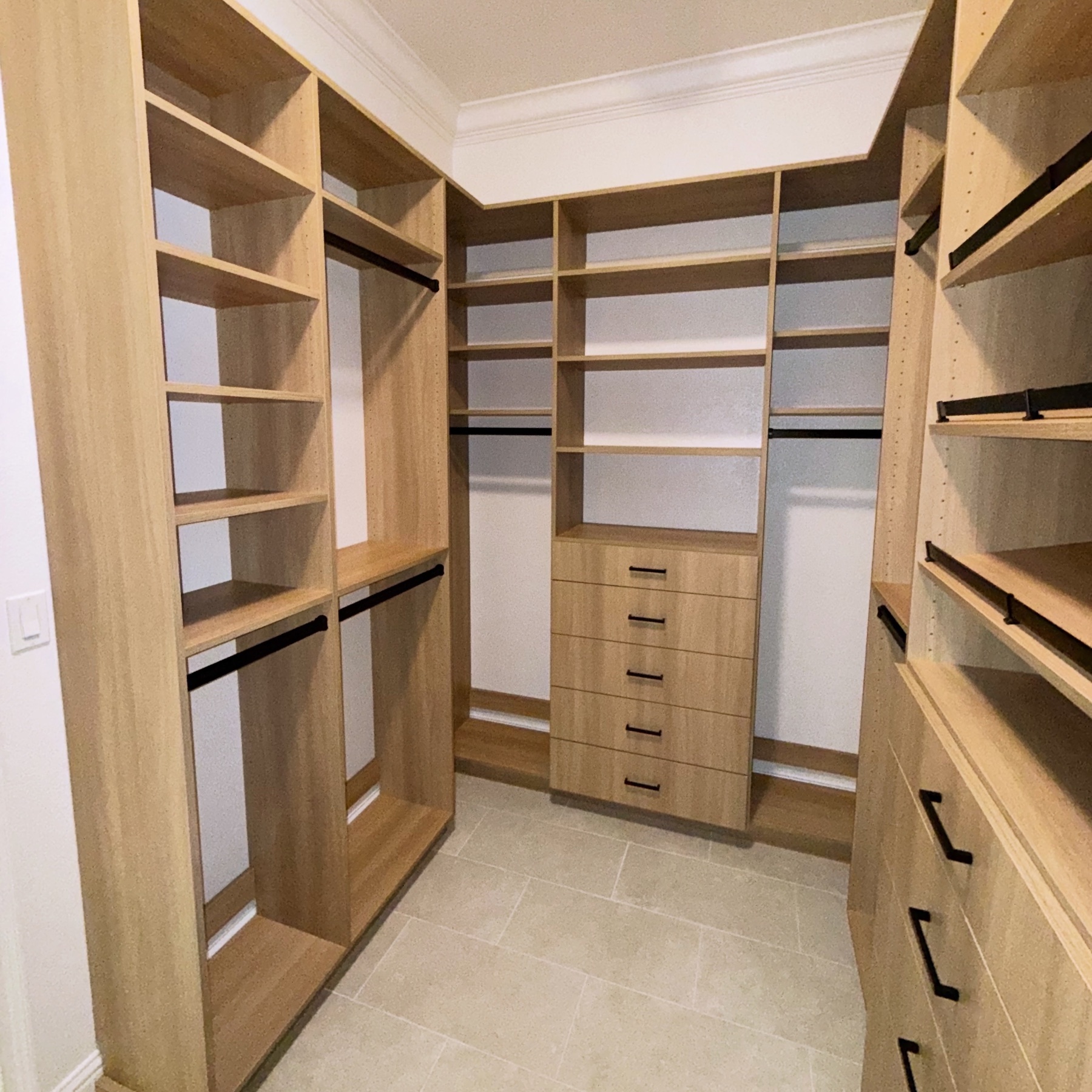 Completed custom walk-in closet with light wood cabinetry and black hardware